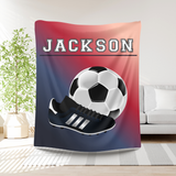 Ombre red to blue throw blanket with the name 'JACKSON' in white varsity font at the top. A big image of a soccer ball and cleat taking up most of the blanket. 