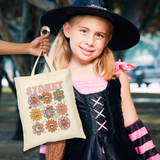 A young girl in a witch costume holds a cream canvas tote bag printed with colorful flowers and the word 'SYDNEY'. The photo is taken outdoors in a blurred park-like setting.