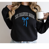 A woman wearing a black crewneck sweatshirt with 'ZZ DANCE MOM' in white outlined letters and a blue bow graphic on the front, holding a white mug.