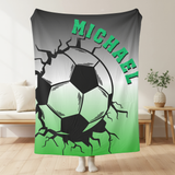 Grey and green throw blanket with image of a soccer ball breaking through with cracks around it. The name Michael in green arched over the top. 