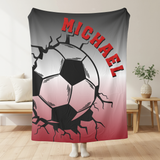 Grey and red throw blanket with image of a soccer ball breaking through with cracks around it. The name Michael in red arched over the top. 