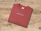 A folded dusty red crewneck t-shirt with the text 'mahj mama.' printed in white lowercase letters, displayed on a light brown wooden background.