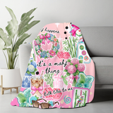 An ombre pink throw blanket with a collage style of all things mahjong. Tiles, flowers, sunglasses, coffee and cute little mahjong phrases like "mahj happens" and "talk tiles to me". The colors are bright and 'preppy' style. The blanket is thrown over a sofa. 