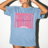 A woman wearing an oversized light blue mineral-wash graphic t-shirt with 'FOOTBALL girlfriend' printed in pink and white on the front.