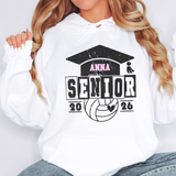 A white pullover hoodie worn by a model, featuring a black distressed graphic of a graduation cap, a volleyball, and the text 'ANNA SENIOR 2026' with a small heart detail.