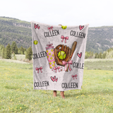 A personalized softball-themed blanket featuring the name 'COLLEEN' repeated, decorated with illustrations of pink bows, pink hearts, yellow softballs, a brown softball glove, and a pink drink cup.