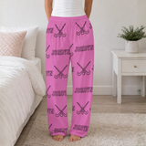 Pink lounge pants with a repeating black and white 'JORDYN' and field hockey sticks, shown on a model standing in a bedroom setting.