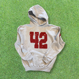 A heather gray pullover hoodie with a distressed red '42' graphic on the front, laid flat on a green grass background.