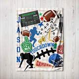 A personalized football-themed blanket featuring a gingham pattern and a collage of sports graphics, including a scoreboard, footballs, a helmet, a foam finger, a megaphone, and the name 'JASON' in blue letters, displayed on a light wood background.