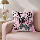 A square pink throw pillow with soccer-themed illustrations and the name 'Nikki' in the center, resting on a light pink armchair in a styled living room setting.