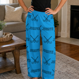 A person wearing bright blue lounge pants with an allover black 'JORDYN' text and crossed field hockey sticks pattern, standing in a living room.