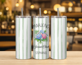 insulated tumblers with clear lids and metal straws sit on a wooden table in a blurred bar or cafe setting. The left and right images have pale green and white vertical stripes, while the center image shows a custom design with the words 'MAHJONG Social Club' and 'STEPHANIE' around an illustration of playing cards and flowers.