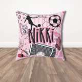 A square pink throw pillow with a soccer-themed graphic design featuring the name 'Nikki' in black, a soccer player silhouette, a soccer ball, a goal net, and goalie gloves, set on a wooden floor against a white wall.