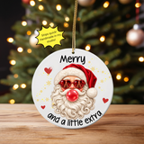 A round white Christmas ornament featuring a cartoon Santa with red heart-shaped sunglasses, a red nose, and the text 'Merry and a little extra,' hanging in front of a blurred Christmas tree with warm lights. A yellow burst says 'Ships quick! Handmade in my studio!'.