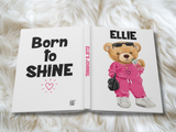 journal, face down, wide open showing back cover that reads 'BORN TO SHINE', on the spine it reads 'ELLIE'S JOURNAL' and the front cover has a teddy bear wearing a hot pink track suit and the name 'ELLIE' in black on the top.