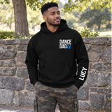 A man wearing a black hoodie with 'DANCE DADZZ' printed on the chest and 'LUCY' on the sleeve, standing outdoors in front of a stone wall.