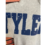 Close-up of a heather gray sweatshirt with large distressed blue block lettering across the chest.