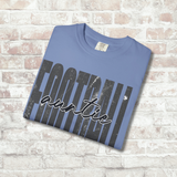 A folded light blue t-shirt with a distressed black graphic reading 'FOOTBALL auntie' is displayed against a white brick wall background.