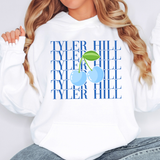 A woman wearing a white hoodie with a blue 'TYLER HILL' text pattern and a light blue cherry graphic on the front, paired with gray jeans.