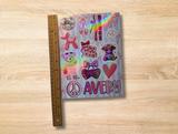 A decorative sticker sheet with a pastel rainbow background and multiple doodle-style graphics, shown standing upright next to a wooden ruler on a light wood surface. The cover includes the name 'AVERY' in pink lettering, hearts, bows, teddy bears, ballet shoes, and a peace sign.