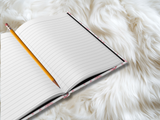 open journal showing lined paper with a pencil down the center. 