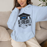 A woman wearing a light blue custom hoodie with a 'Layla Senior 2026' volleyball graphic, sitting on a beige couch.