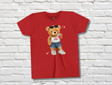 Red t-shirt featuring a cartoon teddy bear wearing sunglasses a white tank top, and denim shorts, with the text "Camp Pontiac" on it's shirt. The bear is holding a pink soft drink and a black hand bag, and wearing white sneakers.