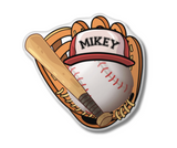 Baseball glove pillow holding a baseball wearing a red hat that has a name, and a baseball bat laying across it. 
