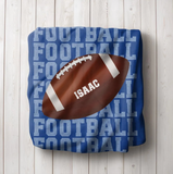 Blue blanket with 'FOOTBALL' on repeat going down the whole blanket, a big football in the center with the name 'ISAAC' on the ball in white. 