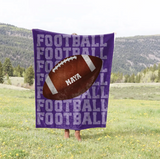 Purple blanket with 'FOOTBALL' on repeat going down the whole blanket, a big football in the center with the name 'MAYA' on the ball in white. 
