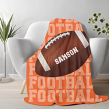 Orange blanket with 'FOOTBALL' on repeat going down the whole blanket, a big football in the center with the name 'SAMSON' on the ball in white. 