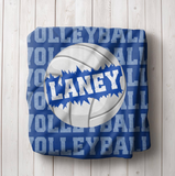 blue  throw blanket with text 'VOLLEYBALL' on repeat down the whole blanket. A big white volleyball in the center, with a name going through the ball. 