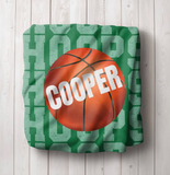 green throw blanket with 'HOOPS' going down the whole blanket on repeat. a big basketball in the center with a name in white going through it. 