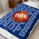 blue throw blanket with 'HOOPS' going down the whole blanket on repeat. a big basketball in the center with a name in white going through it. 