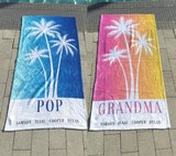 2 Beach towels with palm tree silhouettes, one with blue ombre color, and the other with pink and yellow ombre. The blue towel has 'POP' with 4 grandkids names at the bottom. The pink towel has 'GRANDMA' with the 4 kids names the bottom. 