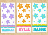 3 Towels all with daisy patterns and names. One towel has lavender daisies, one has orange daisies, and the other has turquoise daisies. 