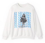 A white crewneck sweatshirt featuring a graphic print of a black-and-white photo of a girl in a tutu, overlaid with repeated blue 'ZZ GRANDMA' text with 'Olivia' in cursive at the bottom.
