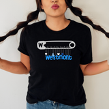 A person wearing a black short-sleeve T-shirt with a graphic print of a safety pin and charms spelling out 'Westmont' in blue, paired with blue jeans against a plain light background.