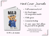 A hard cover personalized journal shown on a pale pink background with printed product details. The journal cover is white with a teddy bear illustration wearing blue clothing and the name 'Mila' at the top.