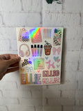 A hand holds a sheet of colorful stickers against a white brick wall. The stickers feature school and lifestyle motifs like a backpack, headphones, a coffee cup, bows, and the name 'ELLIE' in various decorative fonts, with one sticker showing a holographic rainbow effect.