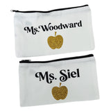 Two white canvas pencil cases with teacher's names and a glittery golden apple. 