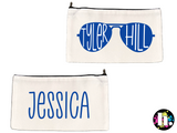 white zippered canvas case, with blue sunglasses on one side, where the camp name is written inside the glasses. the other side has the camper's name also in blue. 